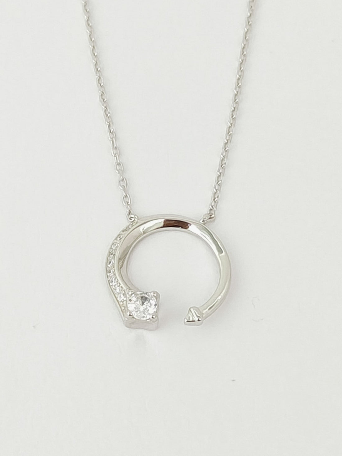 Silver necklace with a circular pendant on a light gray background