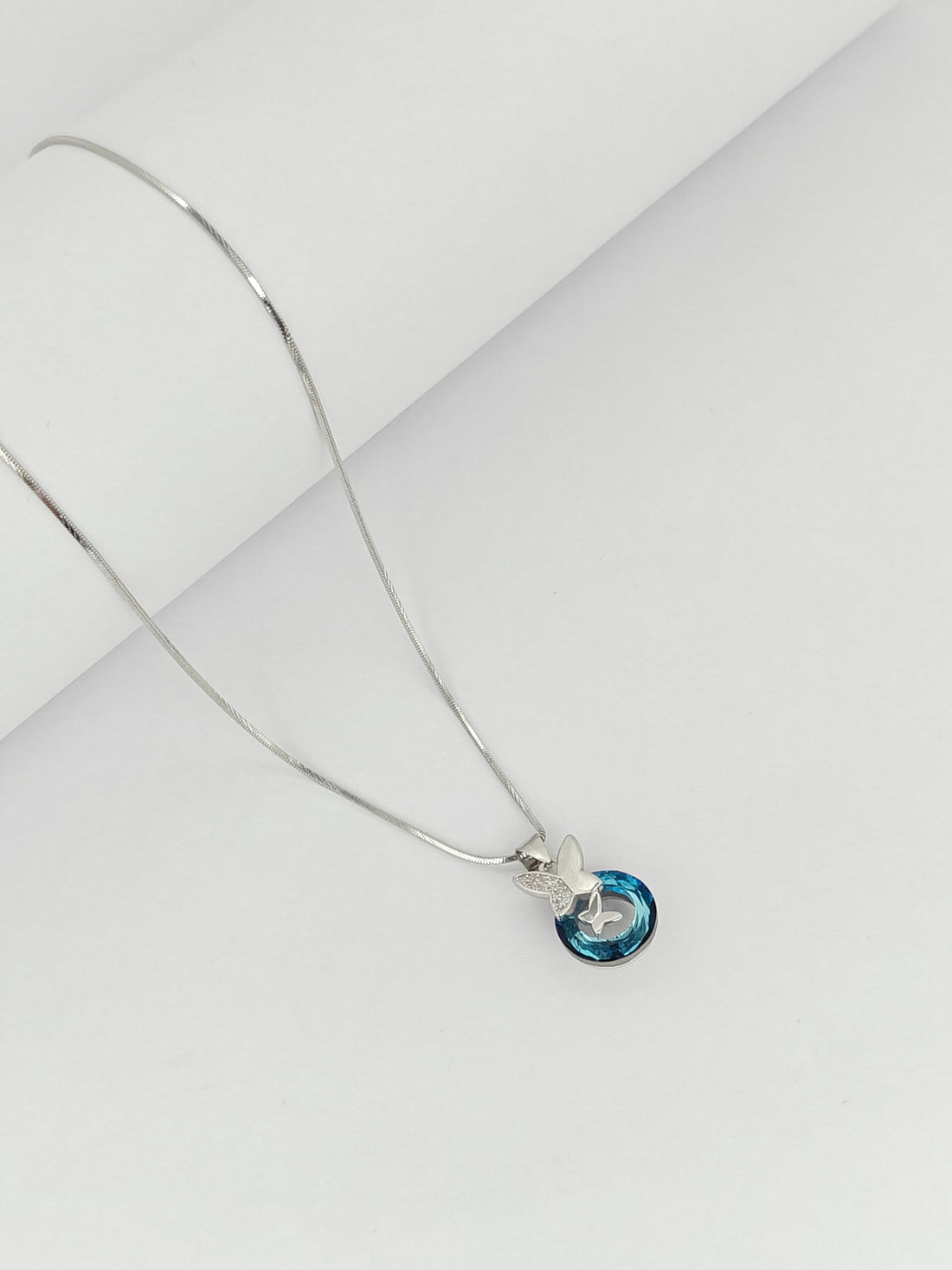 Silver necklace with a blue pendant on a light gray background