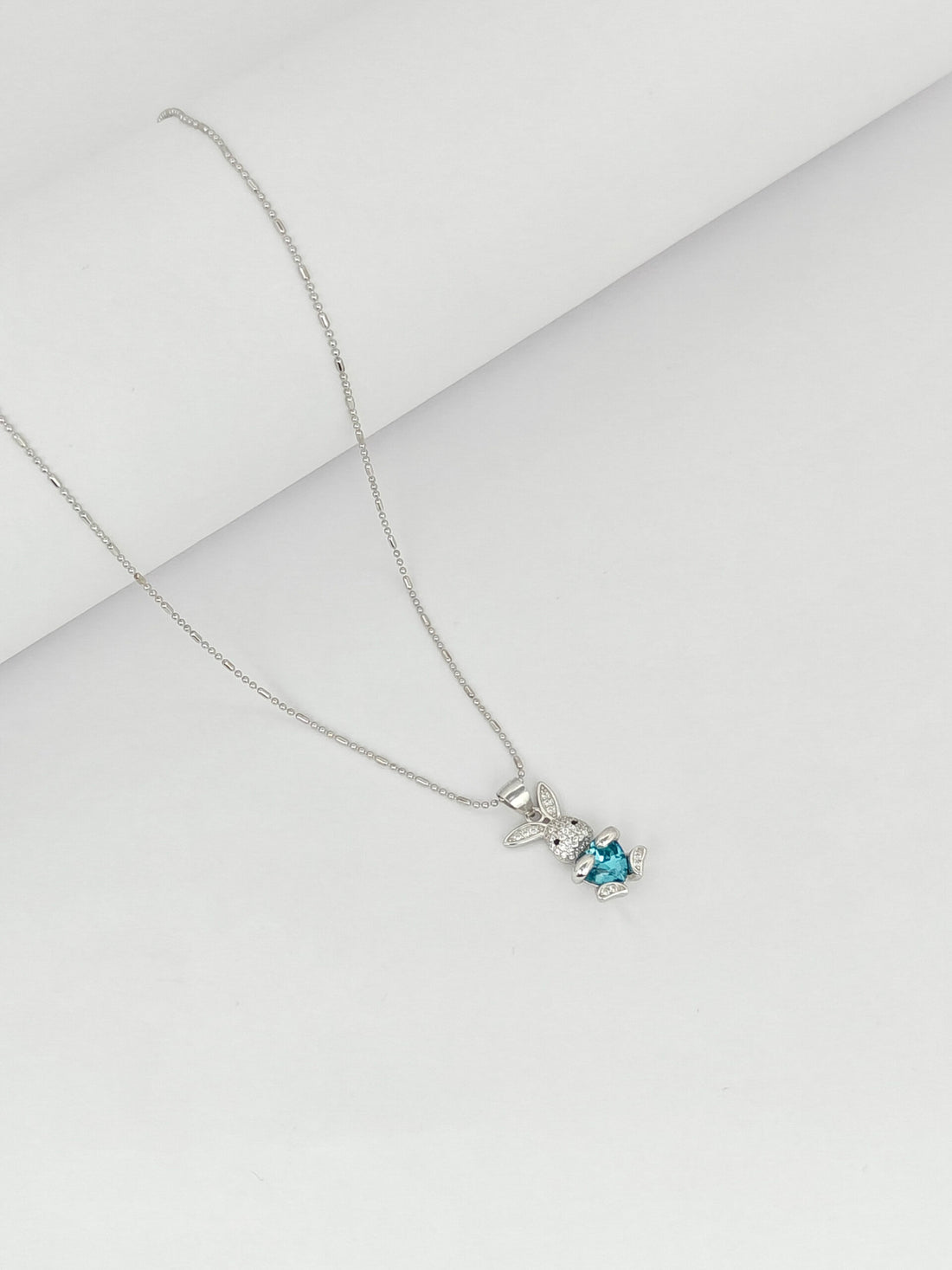 Silver necklace with a blue gemstone pendant on a light gray background