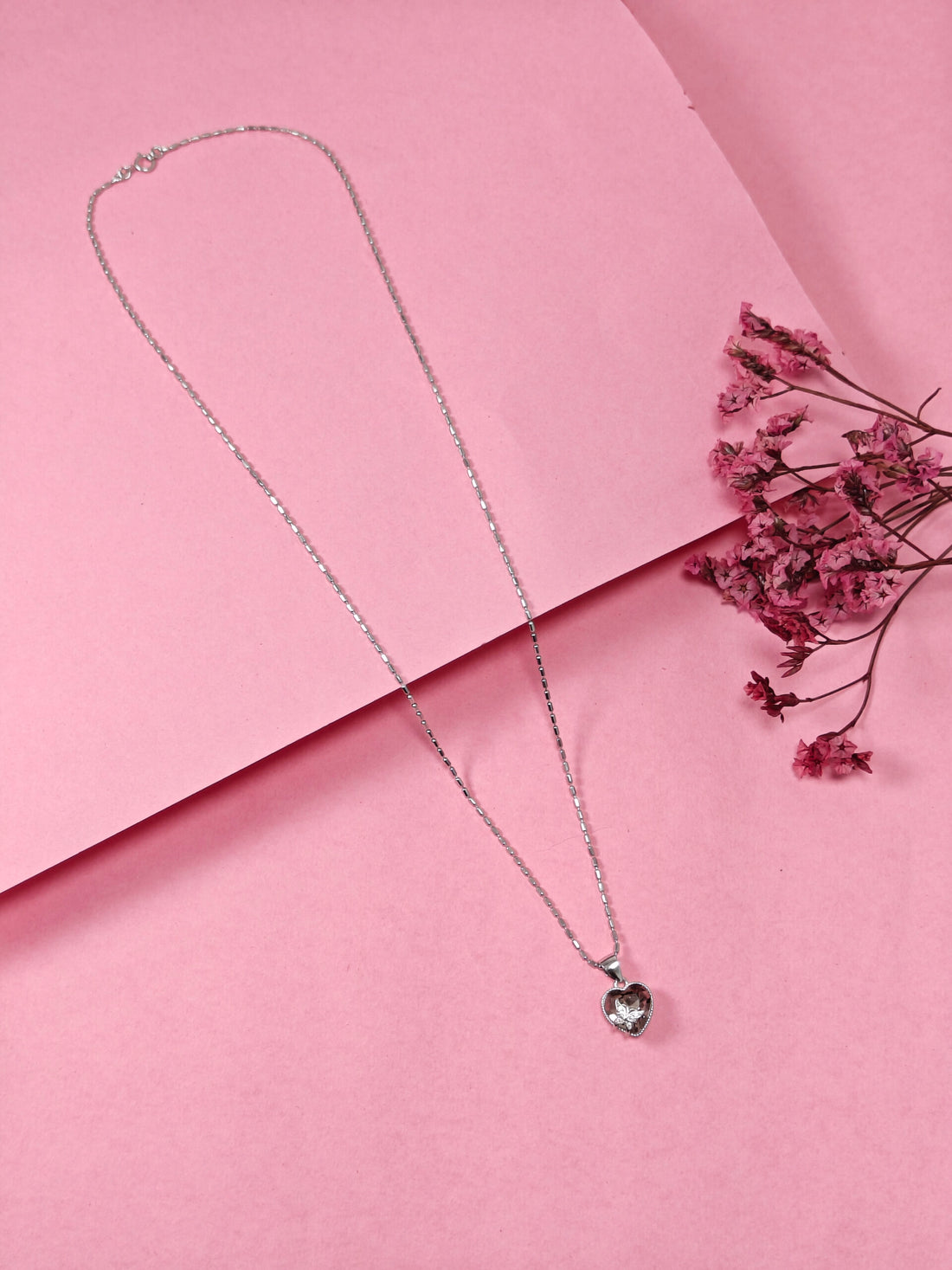 Silver necklace with a heart-shaped pendant on a pink background