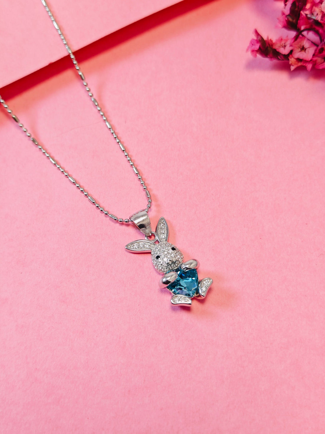 Silver bunny pendant with a blue gemstone on a pink background