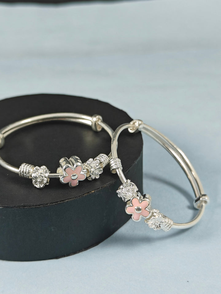 Silver bracelet with floral charms on a black box against a light blue background