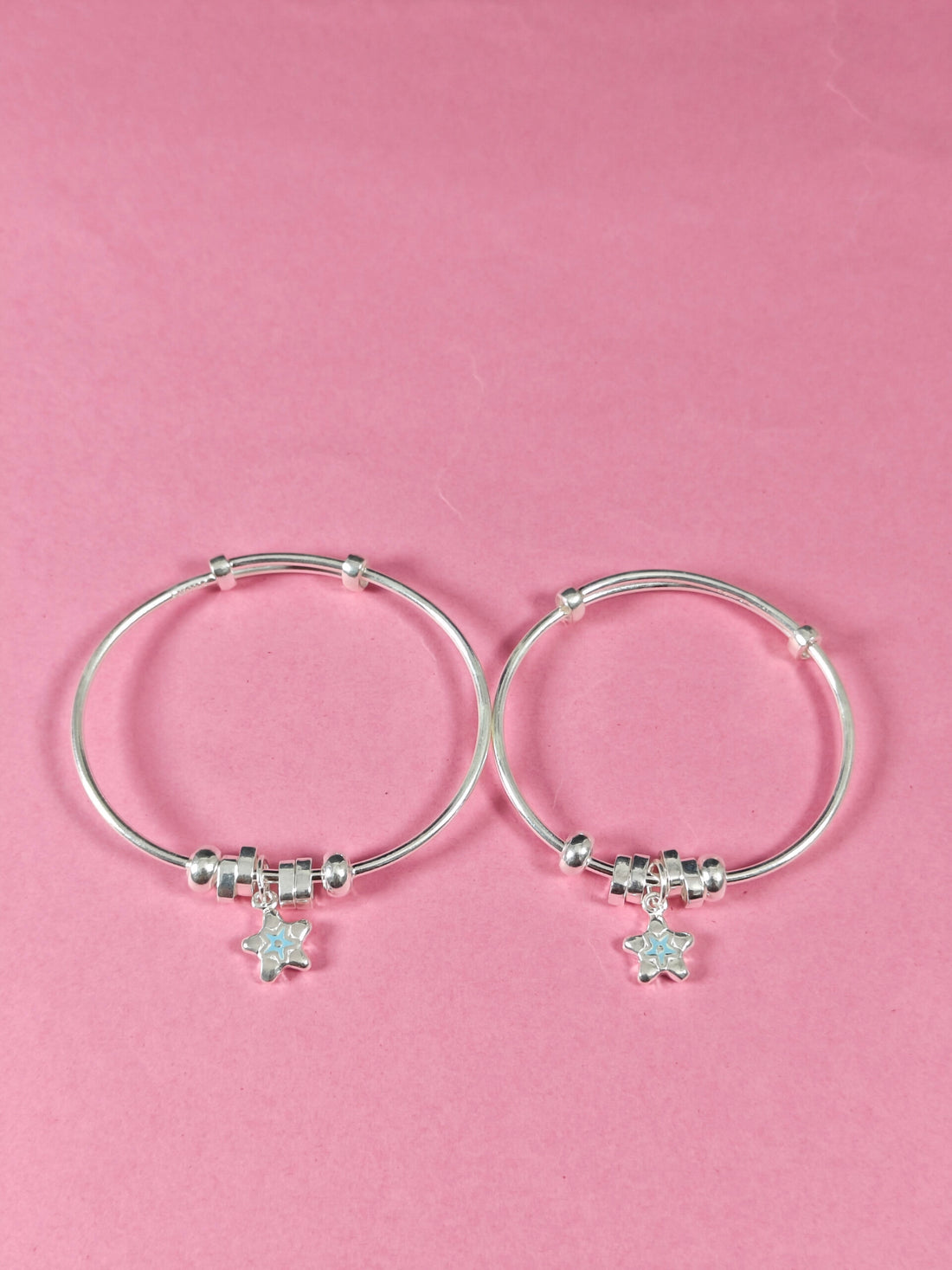 Silver hoop earrings with star charms on a pink background
