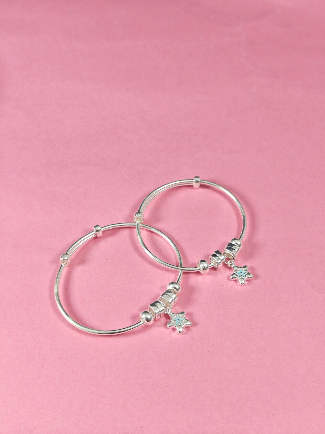 Two silver bangles with turtle charms on a pink background