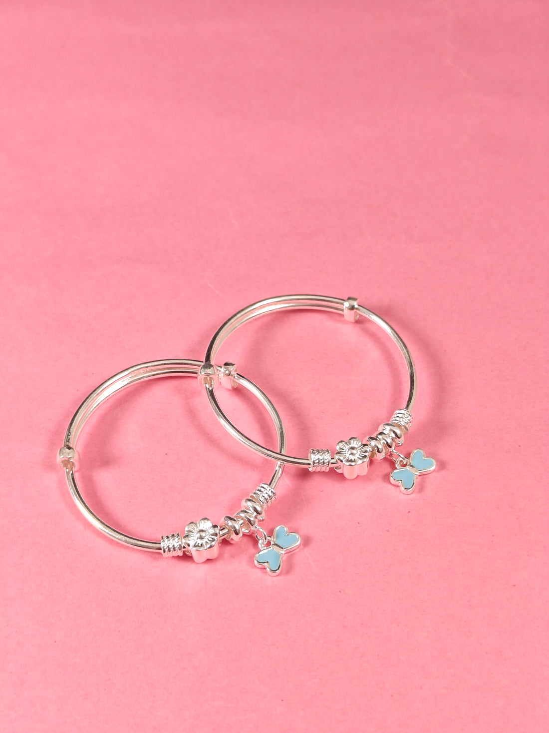 Silver bangles with butterfly charms on a pink background