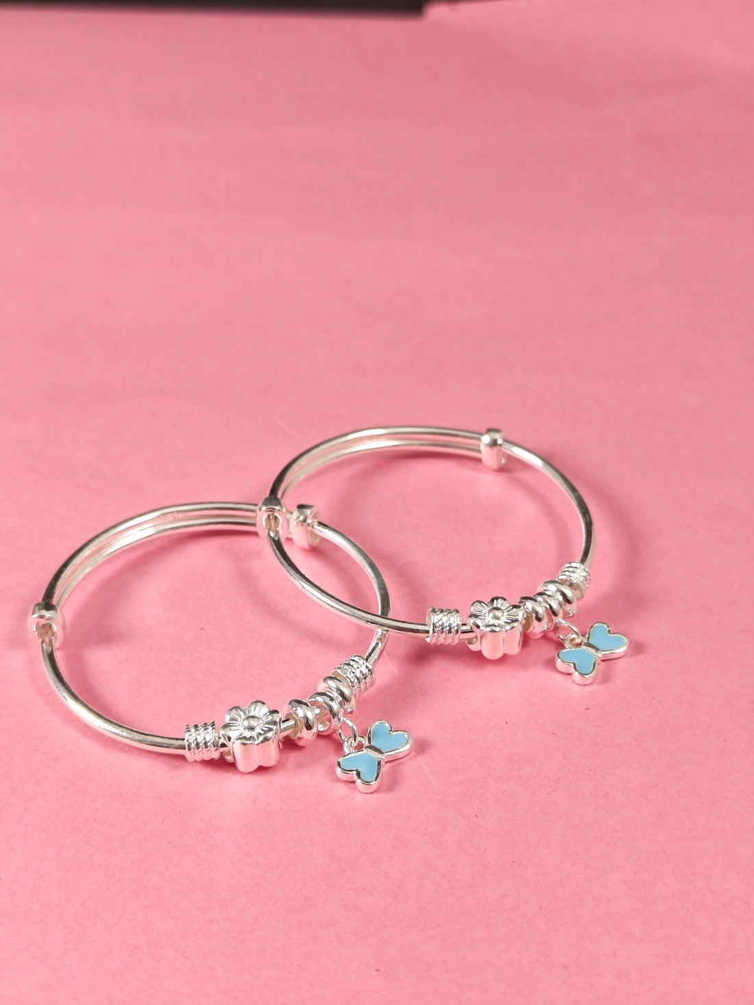 Silver bangle with butterfly charms on a pink background