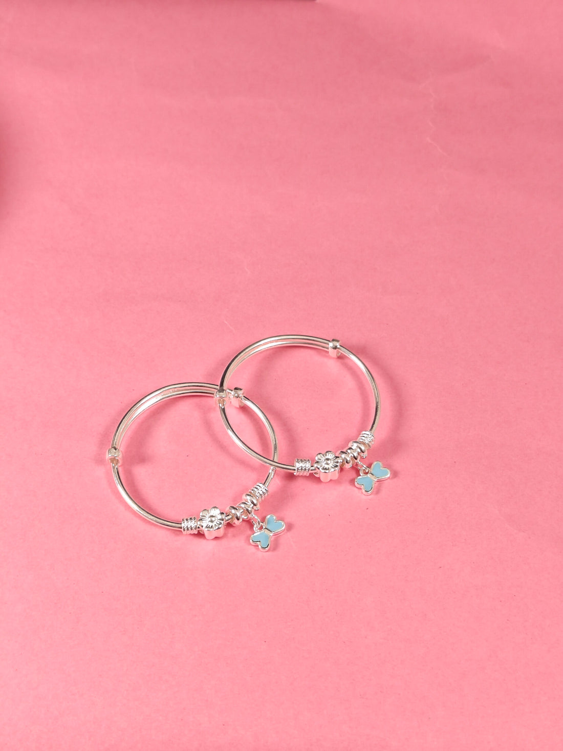 Silver hoop earrings with butterfly charms on a pink background