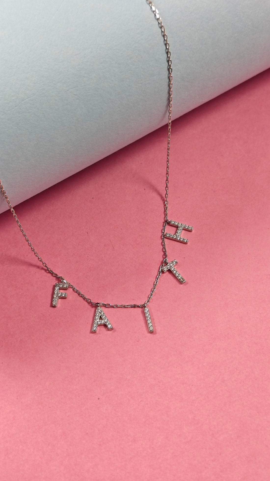 Necklace with diamond-studded letters on a pink background