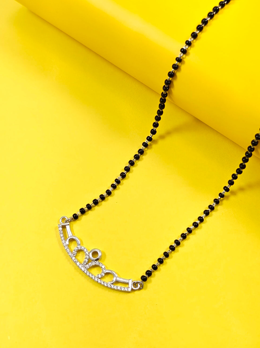 Black beaded necklace with a silver clasp on a yellow background