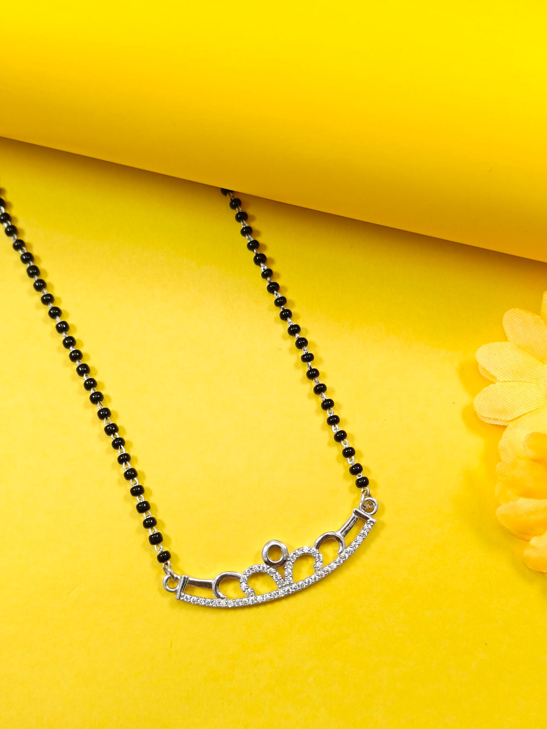 Black beaded necklace with a silver clasp on a yellow background