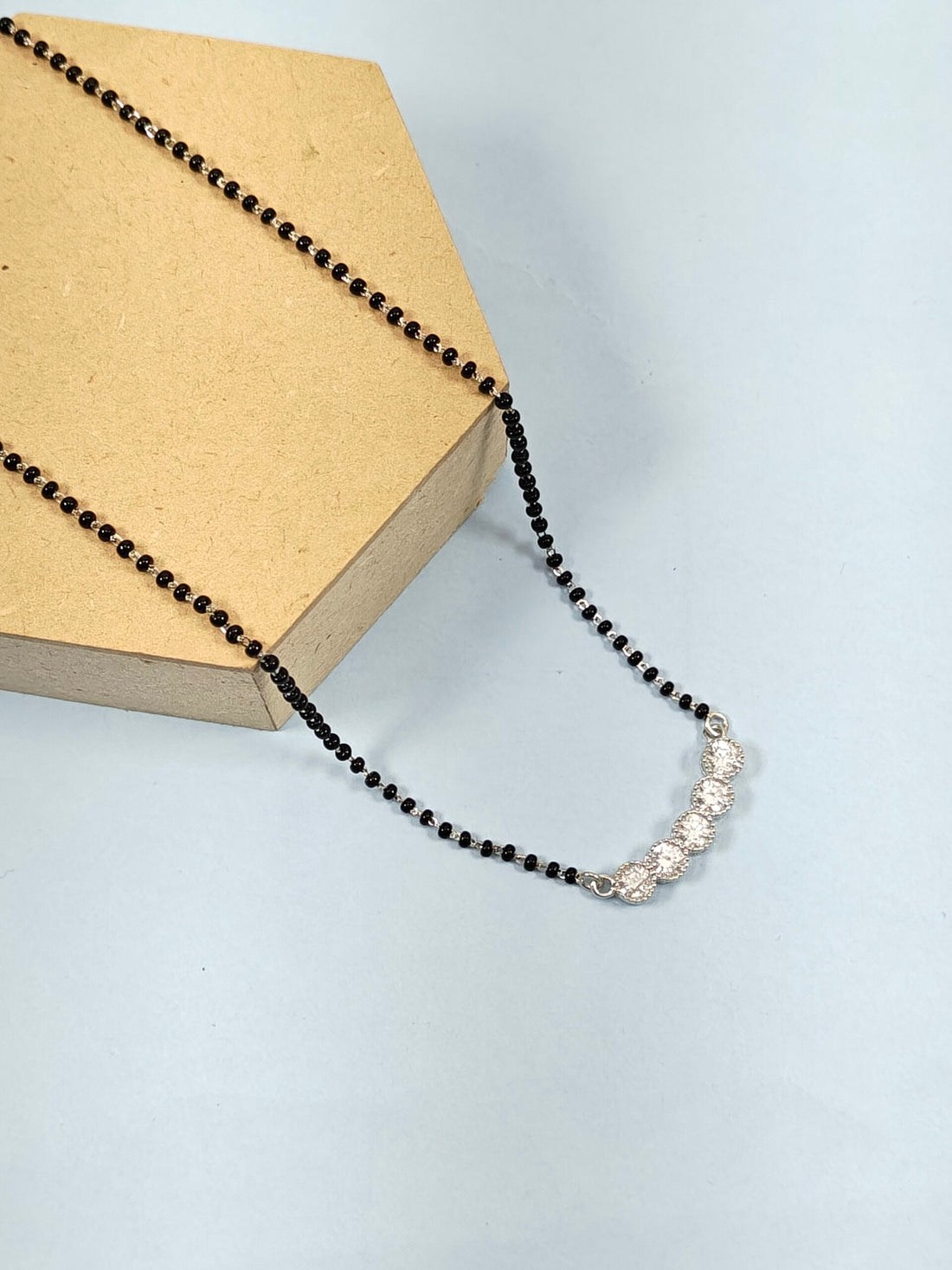 Necklace with black beads and silver clasp on a light blue background