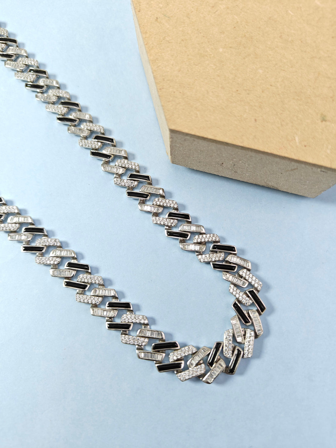 Silver chain necklace on a light blue surface with a beige box in the background
