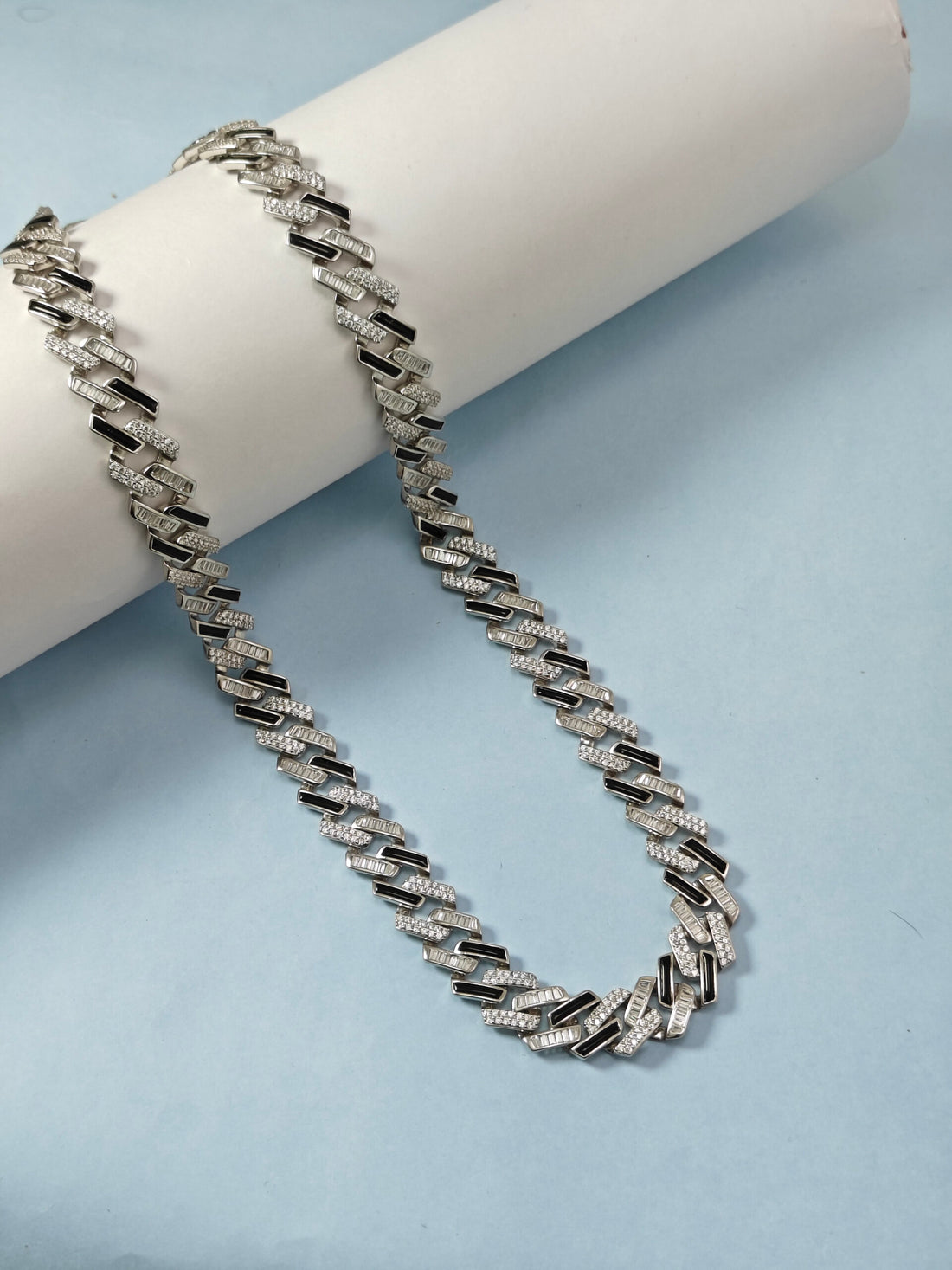 Silver chain necklace on a white cylindrical stand against a light blue background