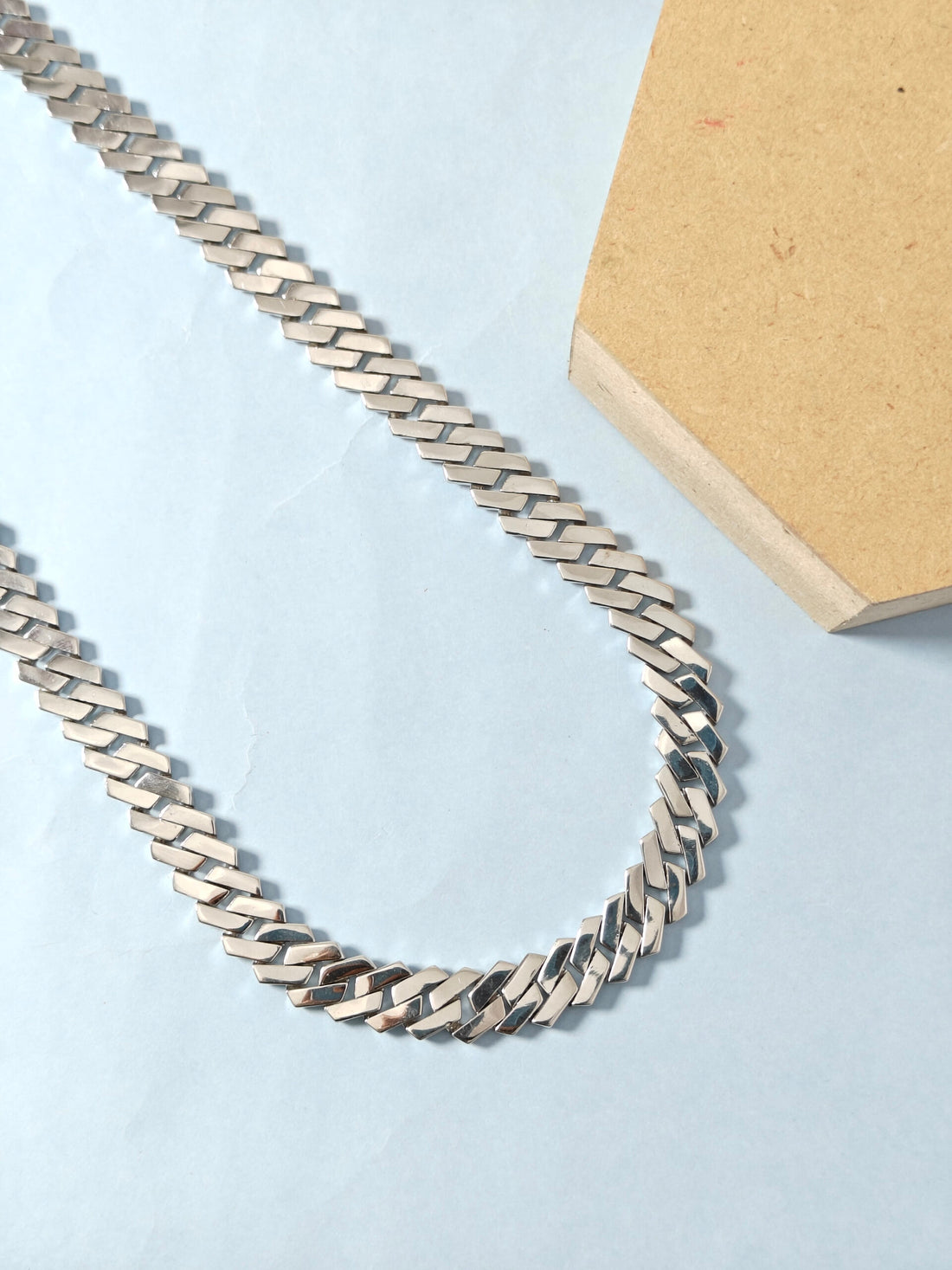 Silver chain necklace on a light blue surface with a cardboard box in the background