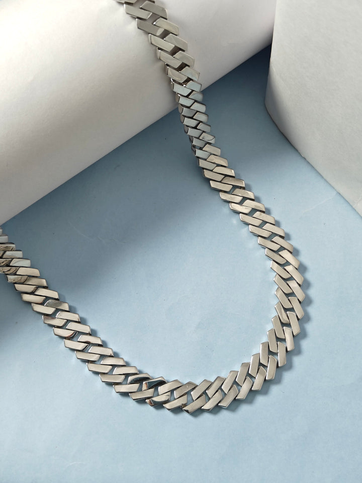 Silver chain necklace on a light blue surface with a white cushion background