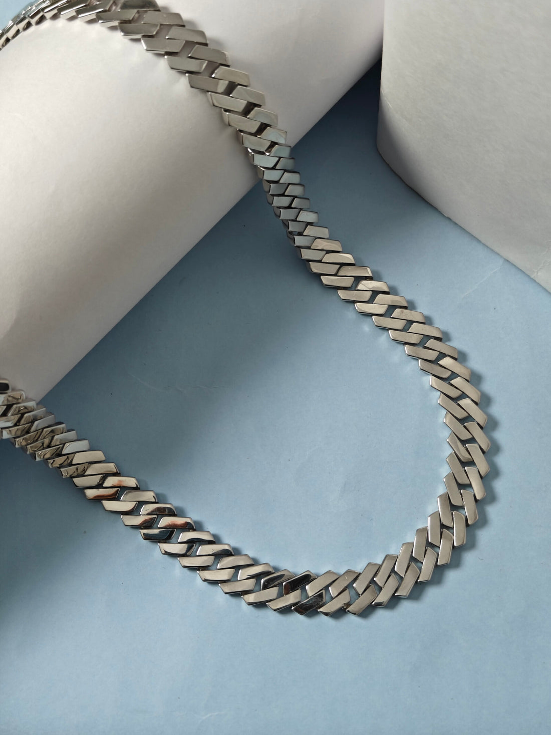 Silver chain necklace on a light blue surface with white cylindrical objects in the background