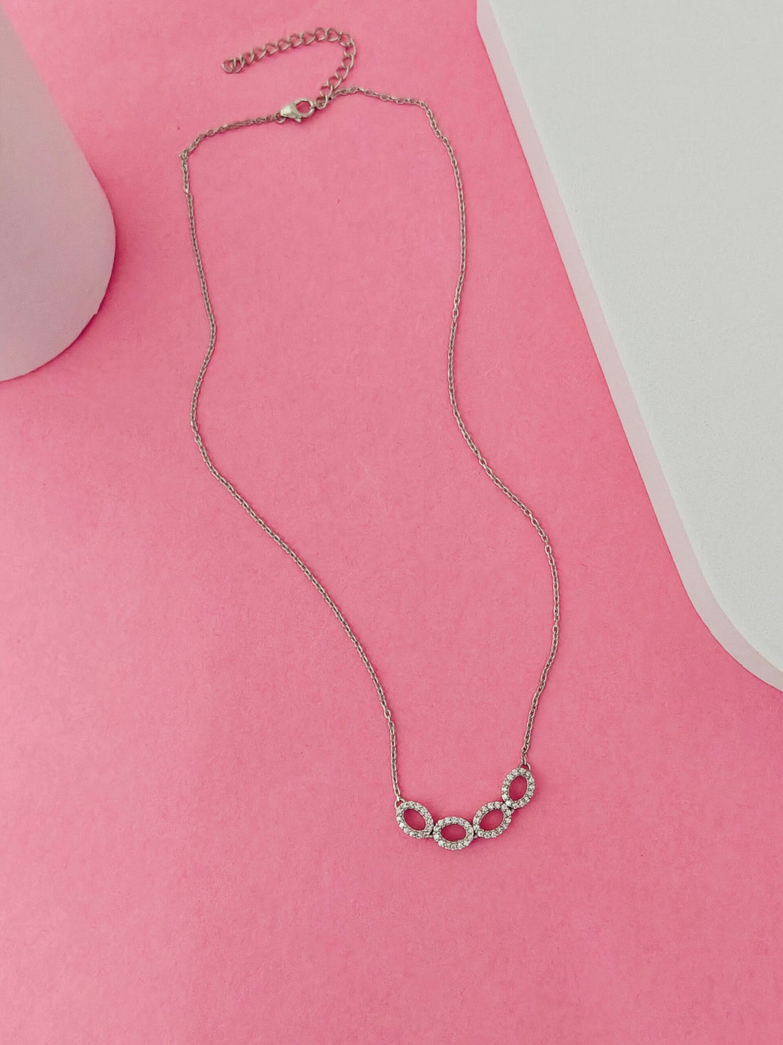 Silver necklace with circular design on a pink surface
