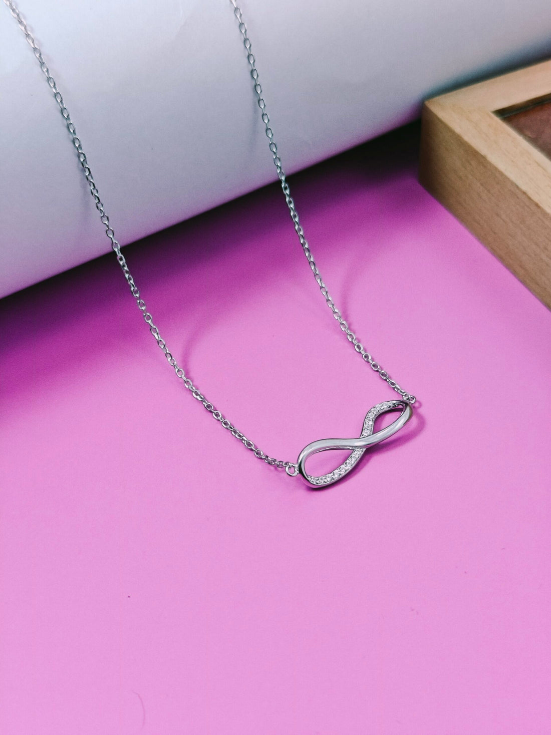 Silver infinity necklace on a pink surface