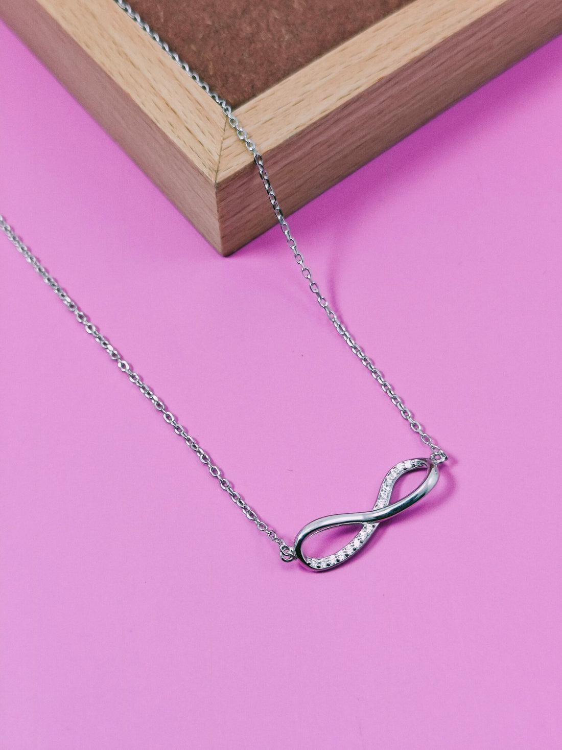 Silver infinity necklace on a pink background