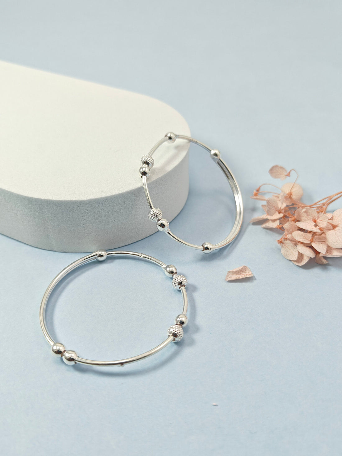 Silver hoop earrings on a light blue background with dried flowers.