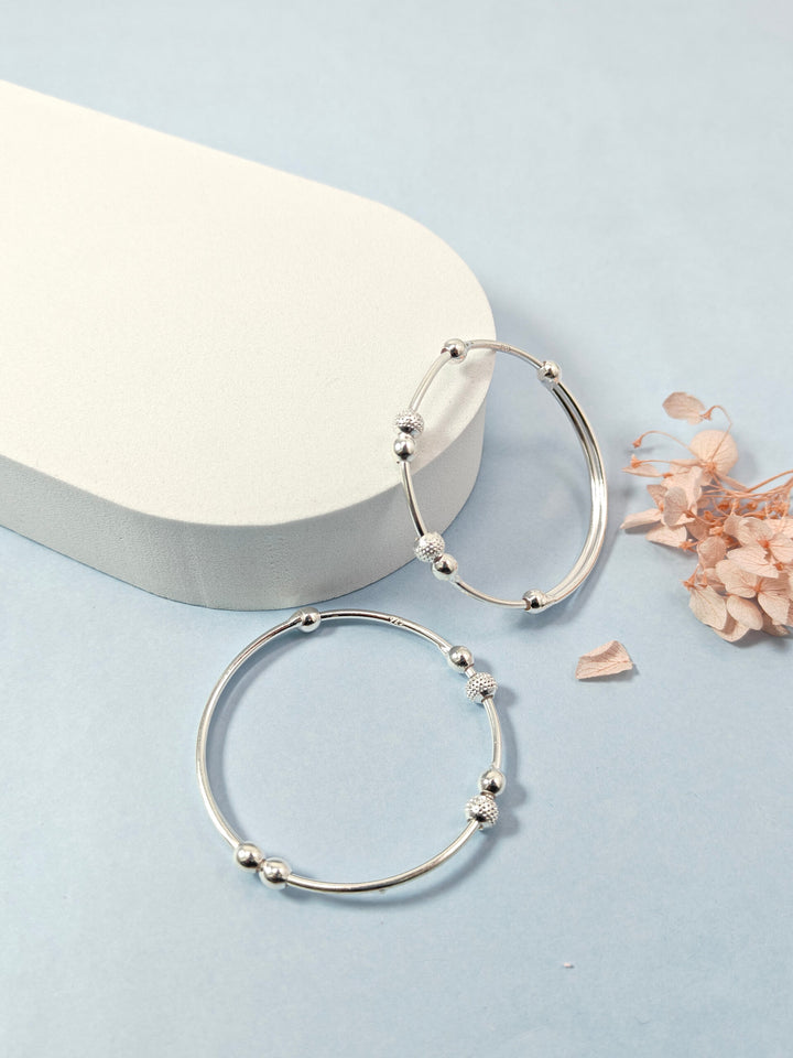 Silver hoop earrings on a light blue background with a white stone and dried flowers.