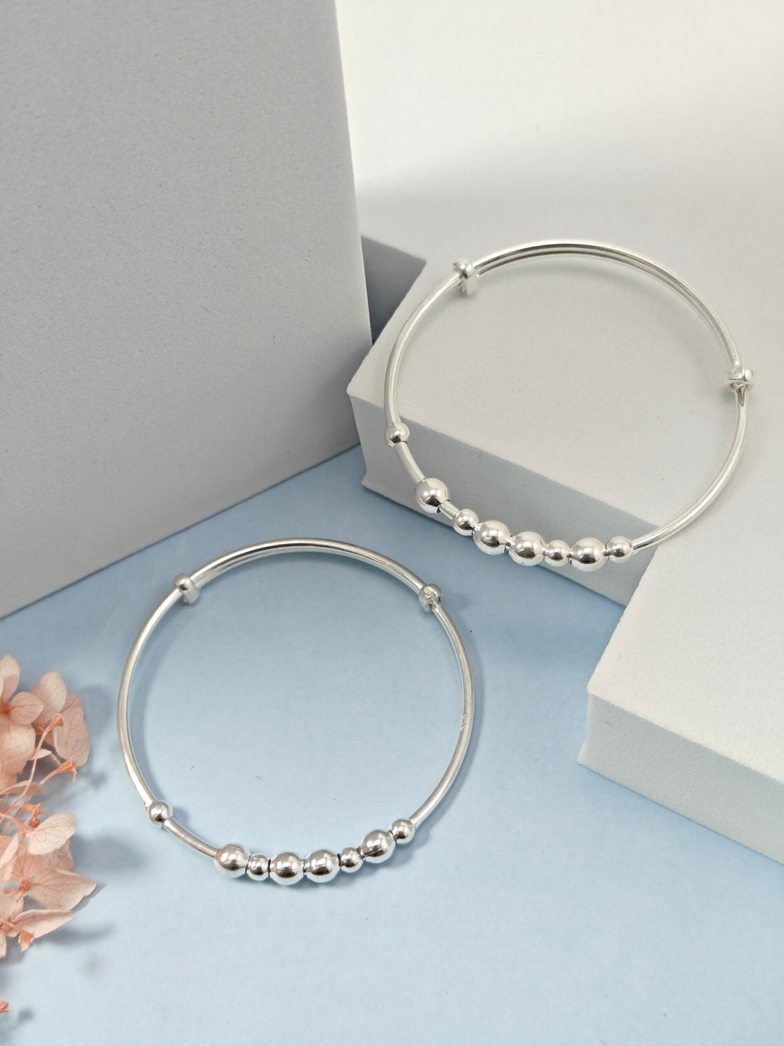 Silver hoop earrings with bead detailing on a light blue surface.