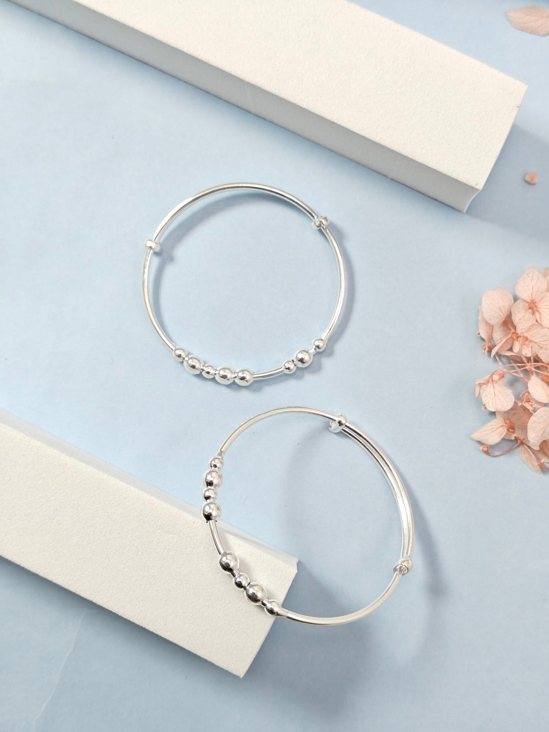 Silver hoop earrings with bead detailing on a light blue surface with flowers.