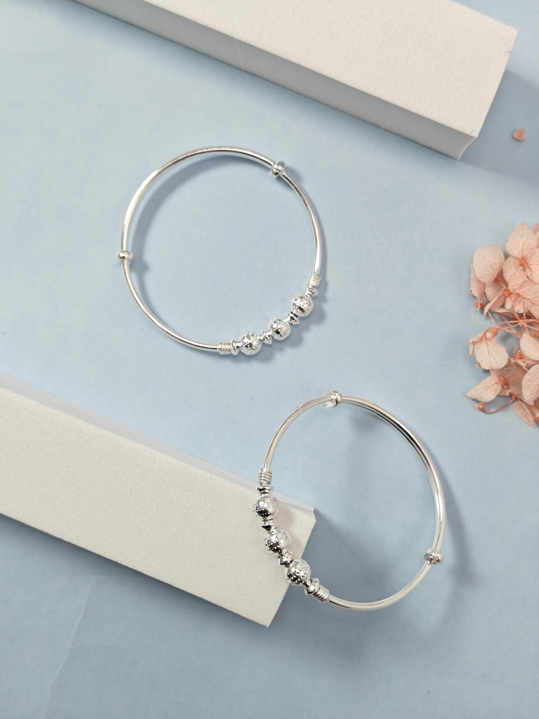 Silver hoop earrings with beads on a light blue surface with dried flowers.