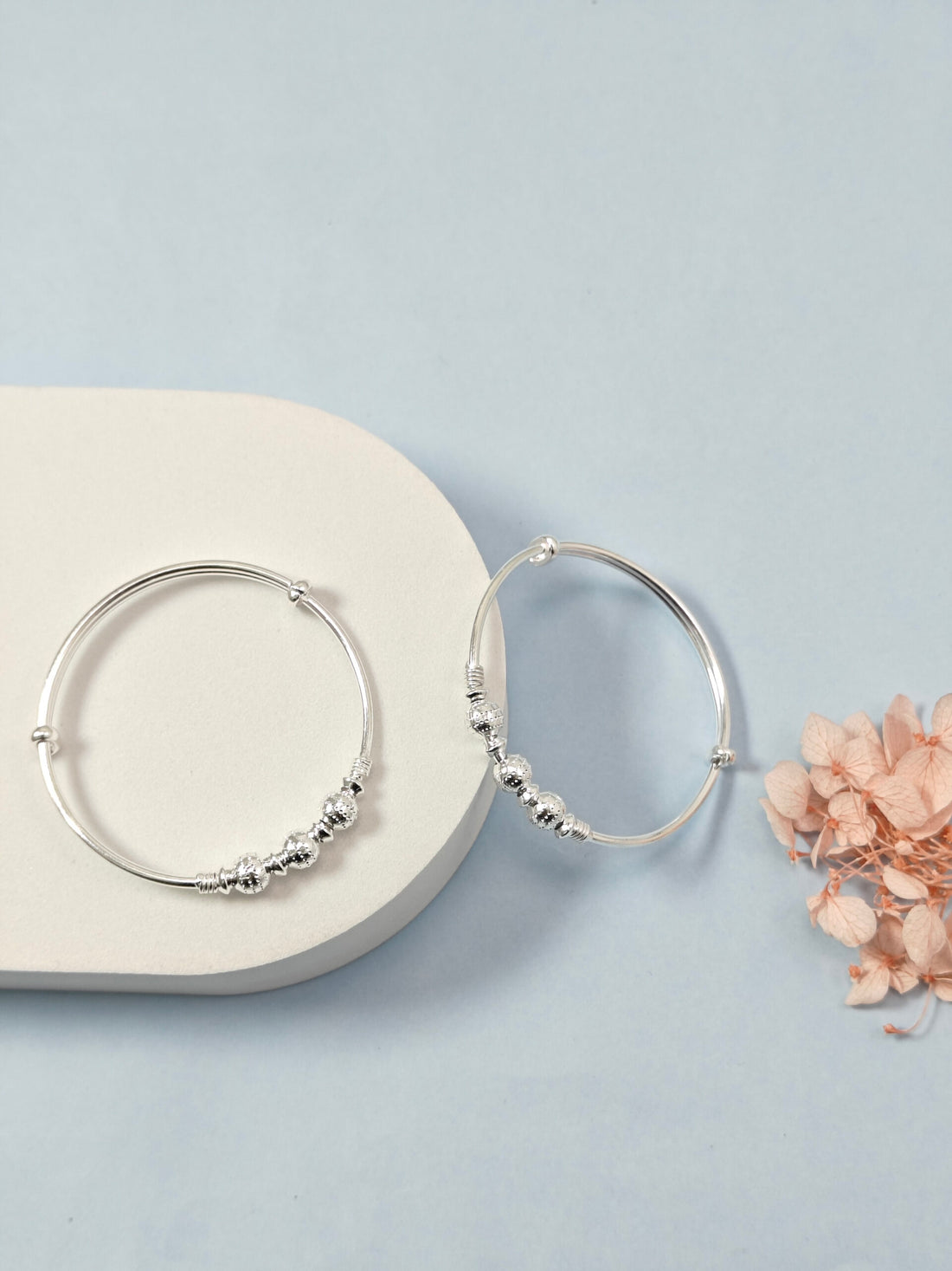 Silver hoop earrings with bead detailing on a light blue background