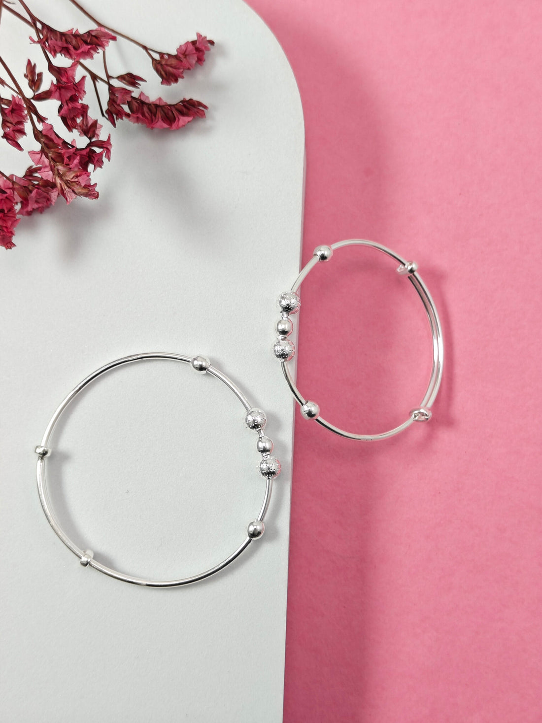 Silver hoop earrings on a pink and white background with dried flowers.