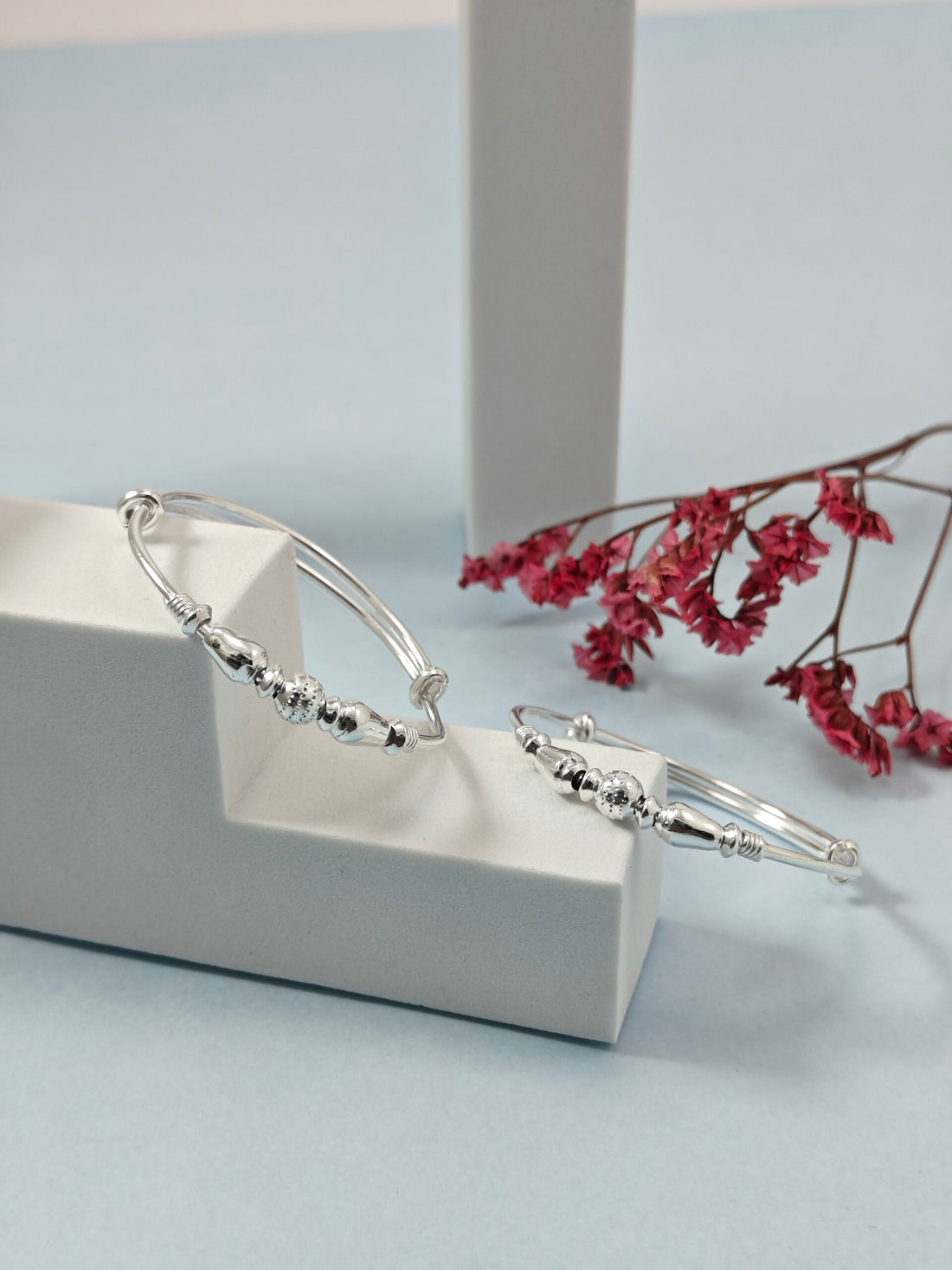 Silver bracelet on a white stand with pink flowers in the background
