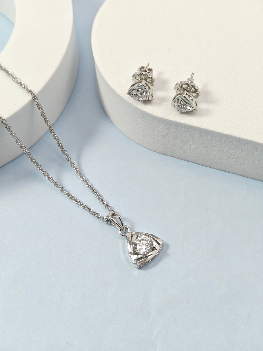 Silver necklace with heart-shaped pendant and matching earrings on a light blue background