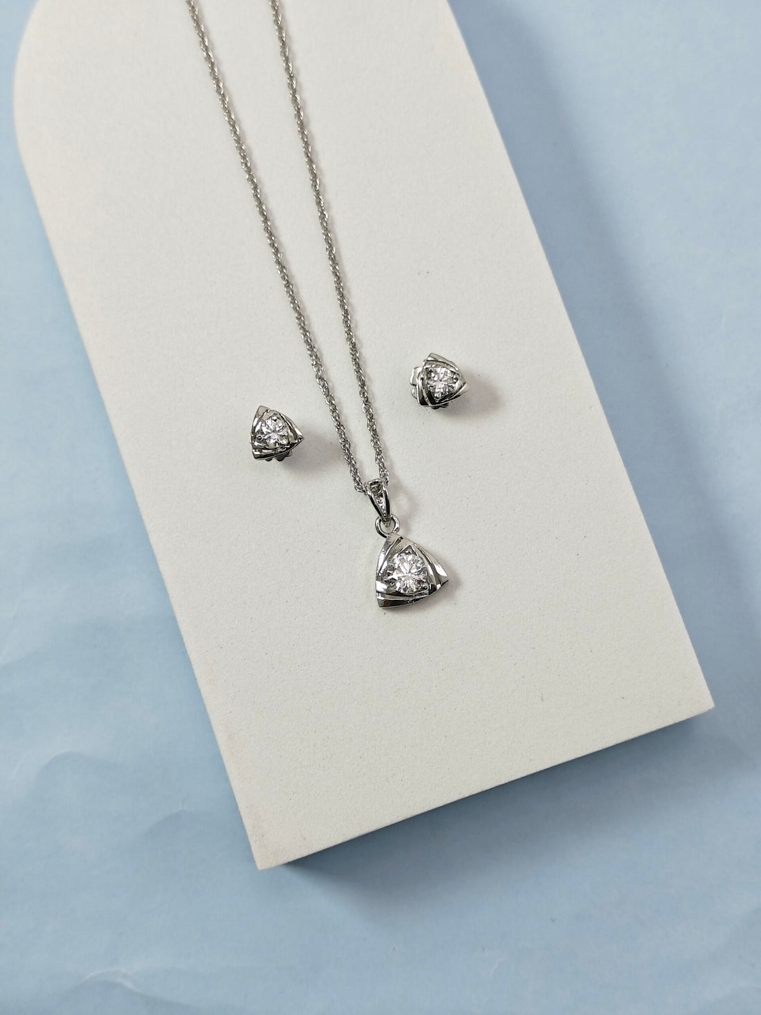 Silver necklace and earrings on a white card with a light blue background