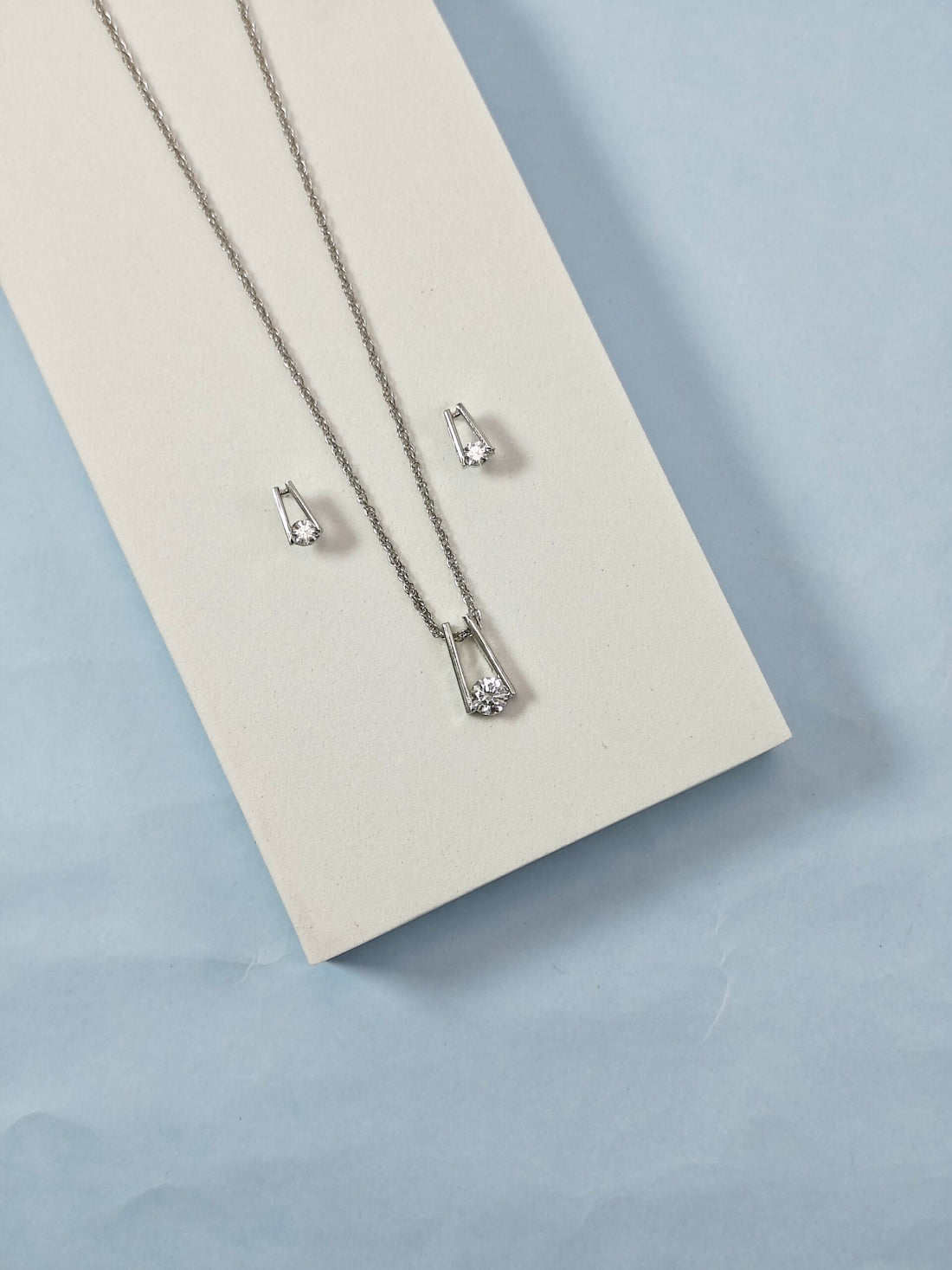 Silver necklace and earrings on a light gray background