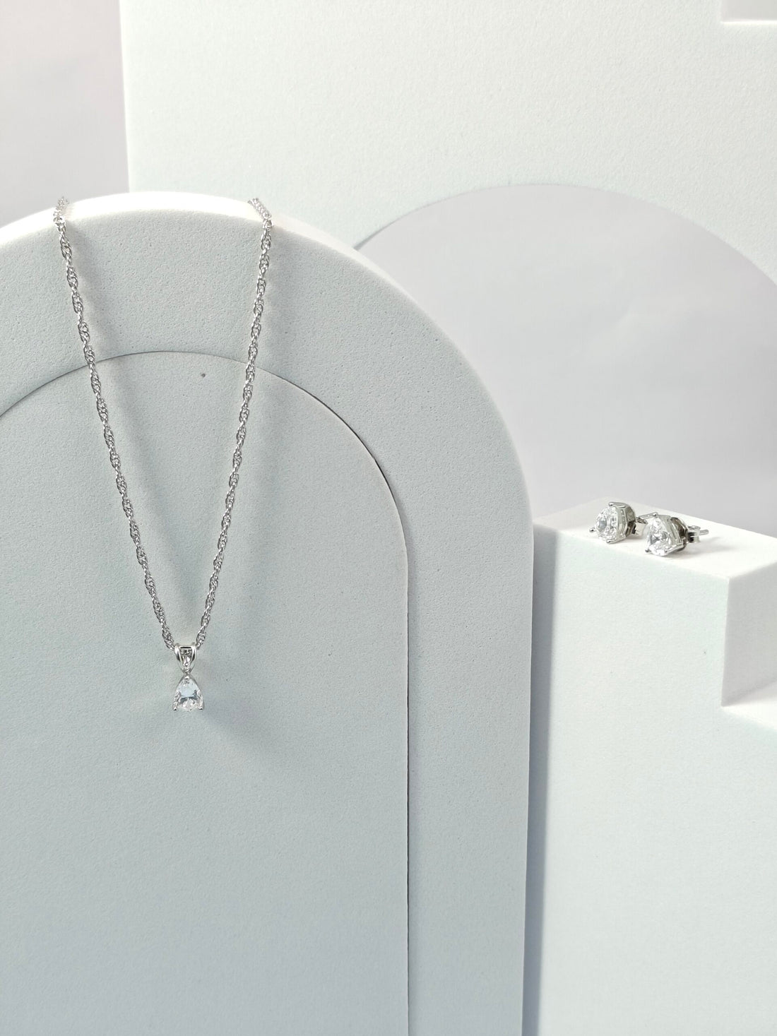 Silver necklace and earrings on a white stand with a white background
