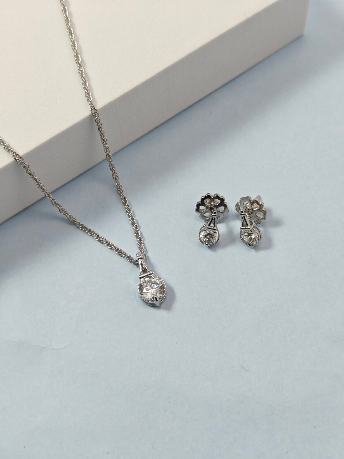 Silver necklace and earrings on a light blue surface