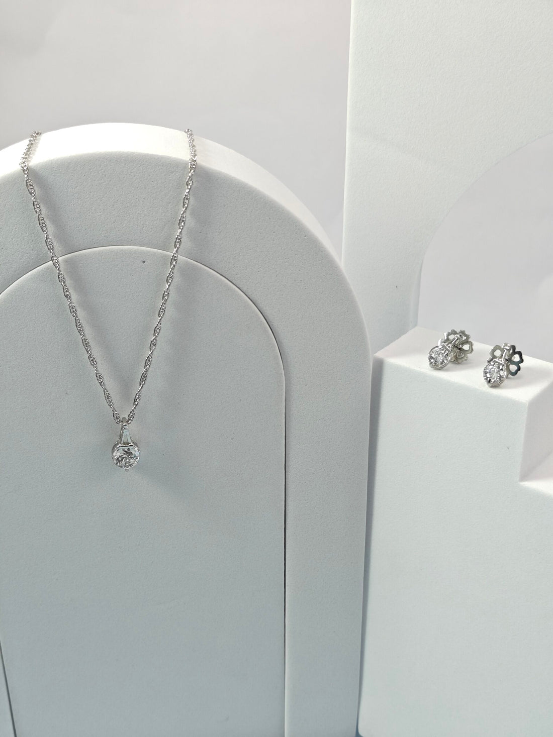 Silver necklace and earrings on a white stand against a white background