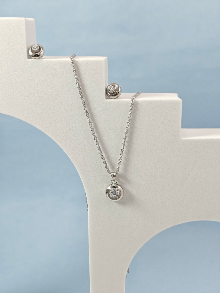 Silver necklace with a pendant on a white stand against a light blue background