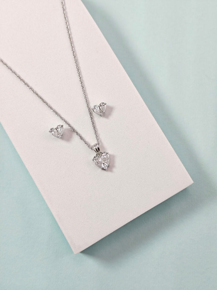 Silver necklace and earrings on a light pink card with a light blue background