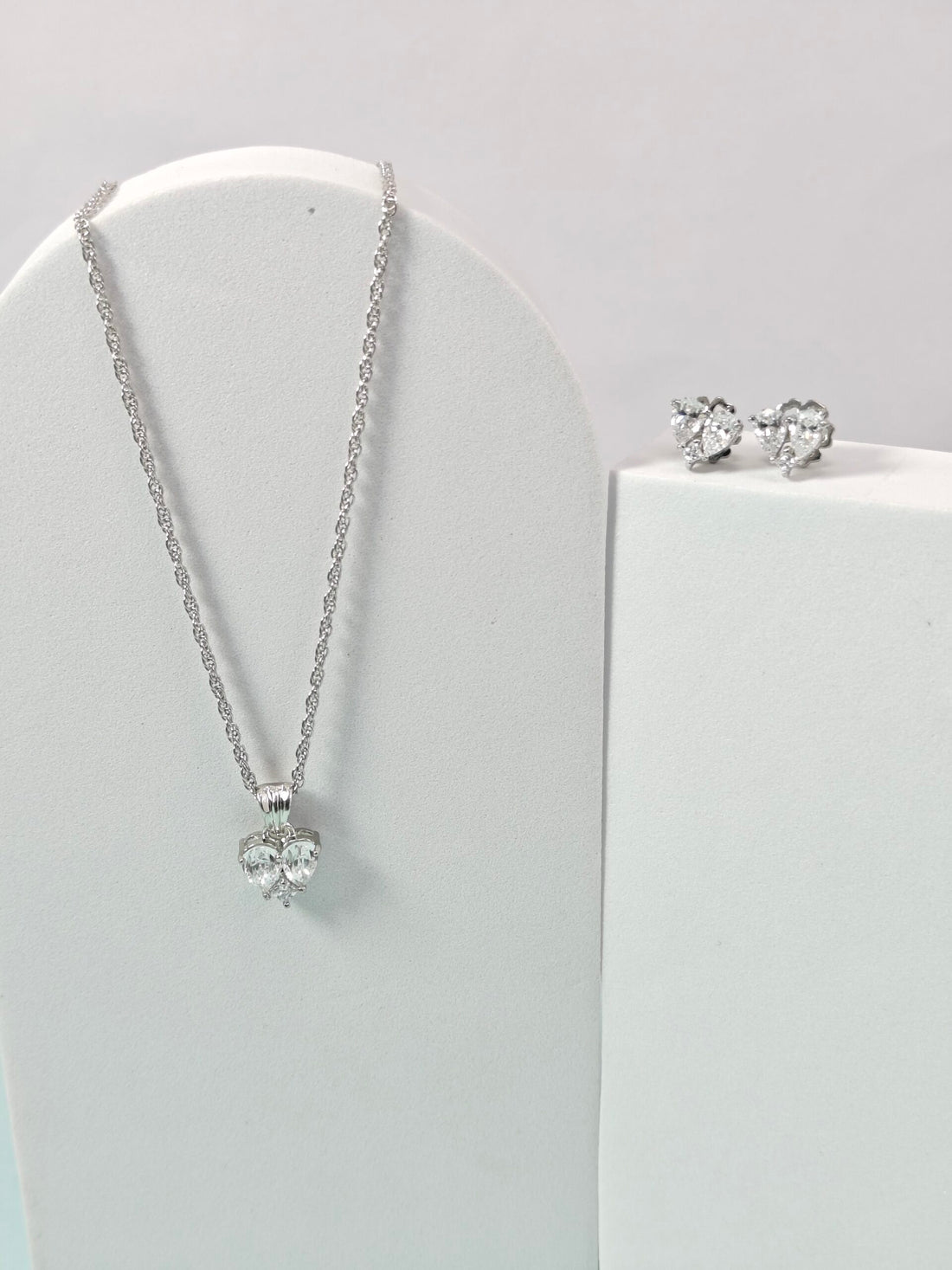 Silver necklace and earrings on a white stand with a light gray background