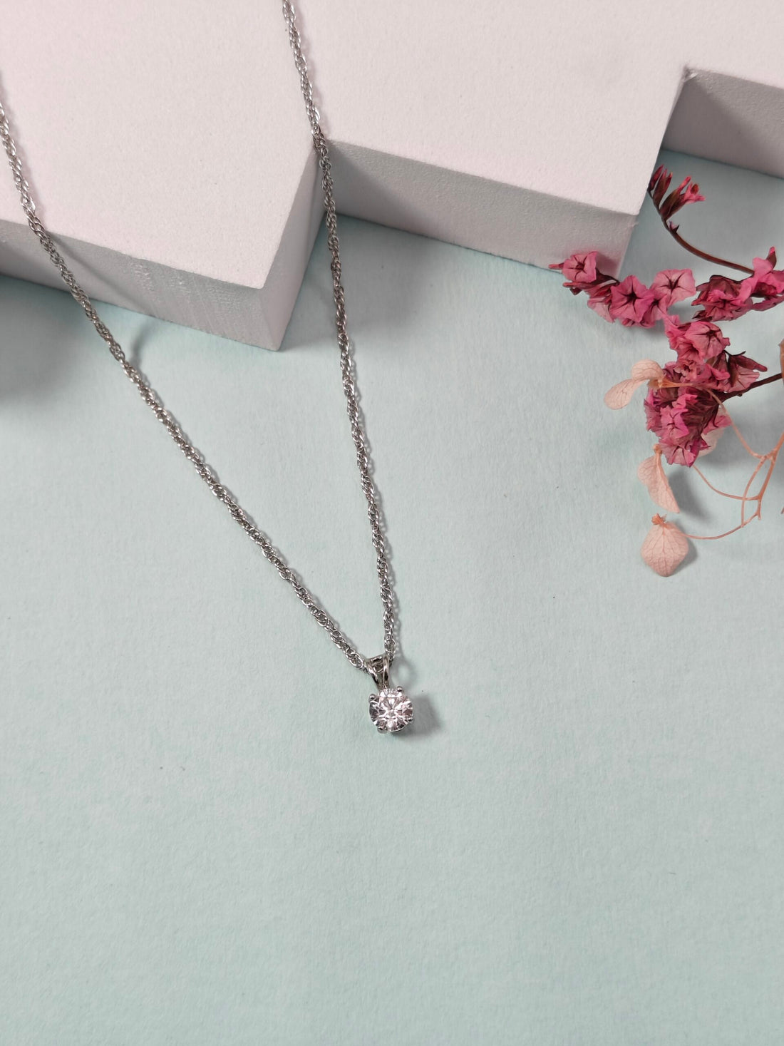 Necklace with a pendant on a light blue surface with pink flowers