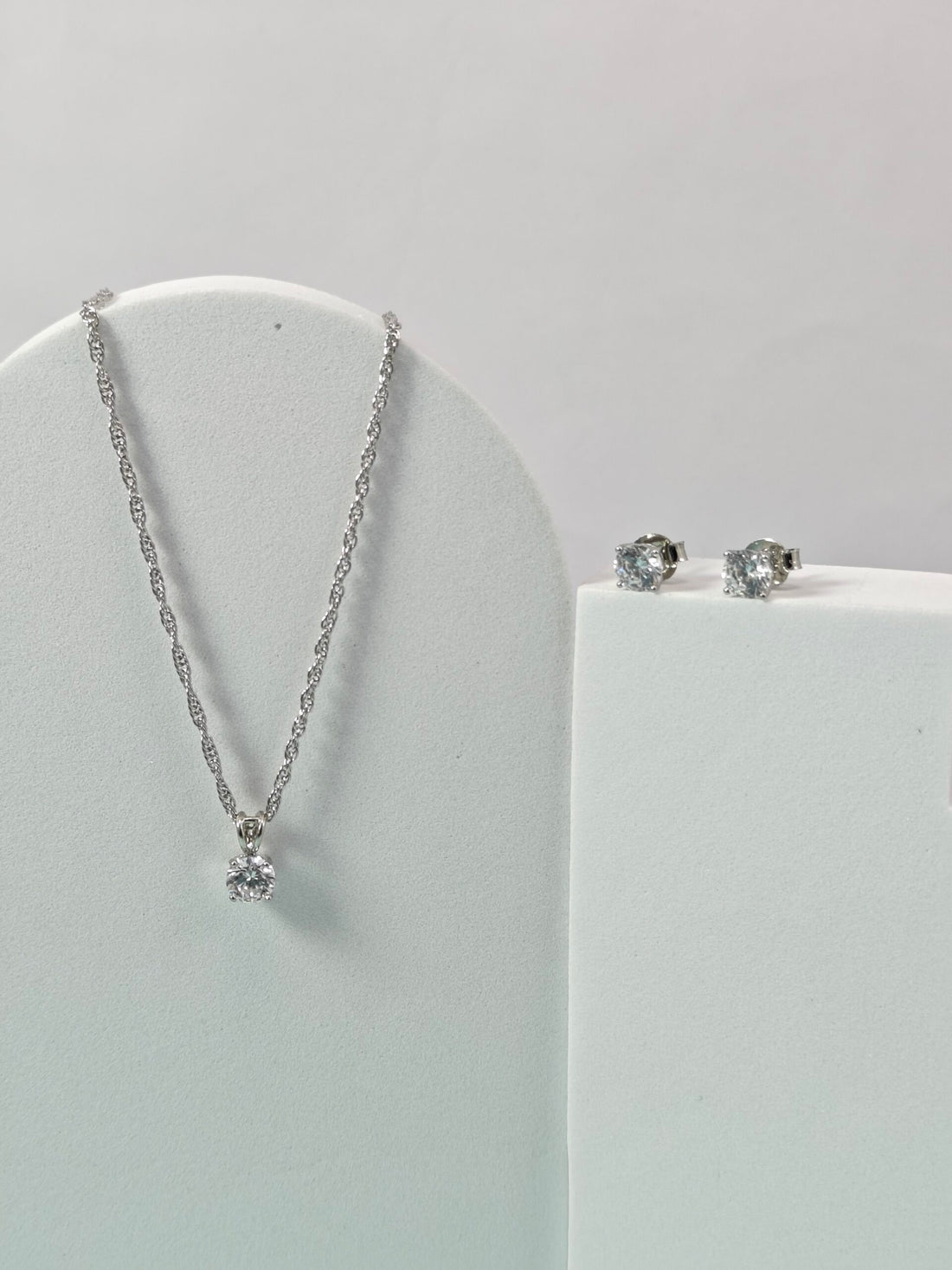 Silver necklace and earrings on a white stand against a light gray background