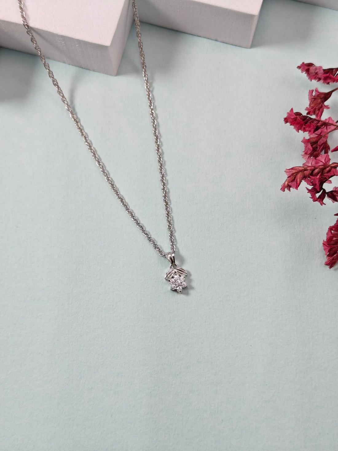 Silver necklace with a pendant on a light gray surface with dried pink flowers.