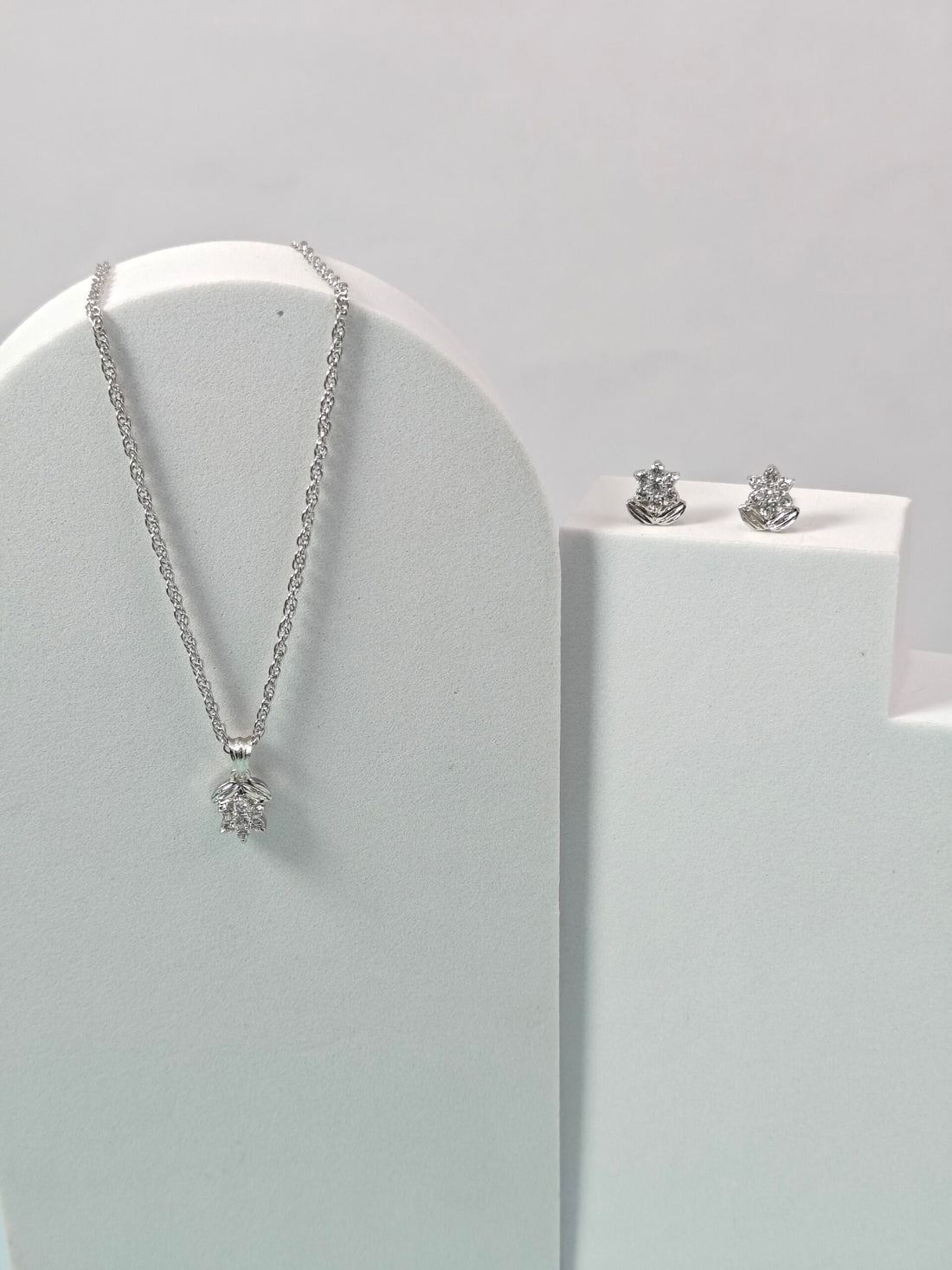 Silver necklace and earrings on a white stand against a light gray background
