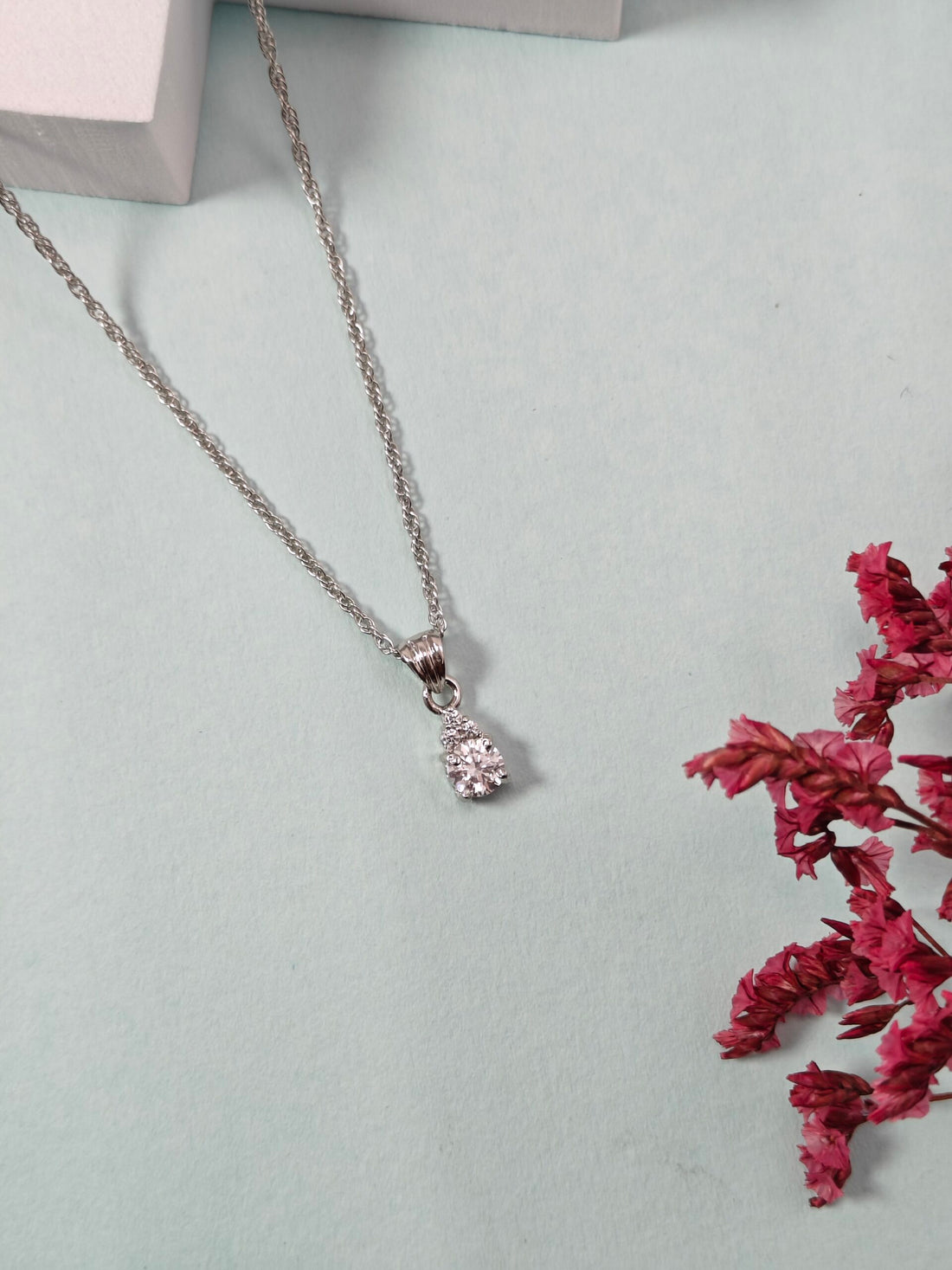 Silver necklace with a pendant on a light blue surface with pink flowers.