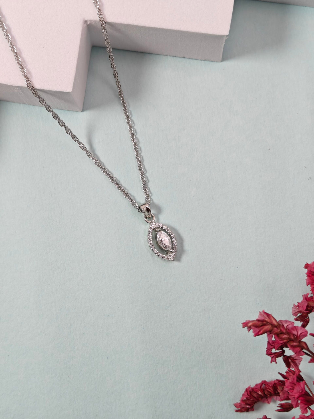Silver necklace with a pink gemstone pendant on a light blue background with pink flowers.