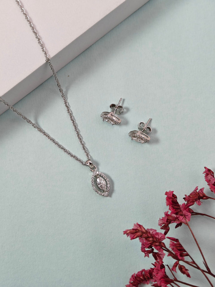 Silver necklace and earrings on a light gray surface with pink flowers.