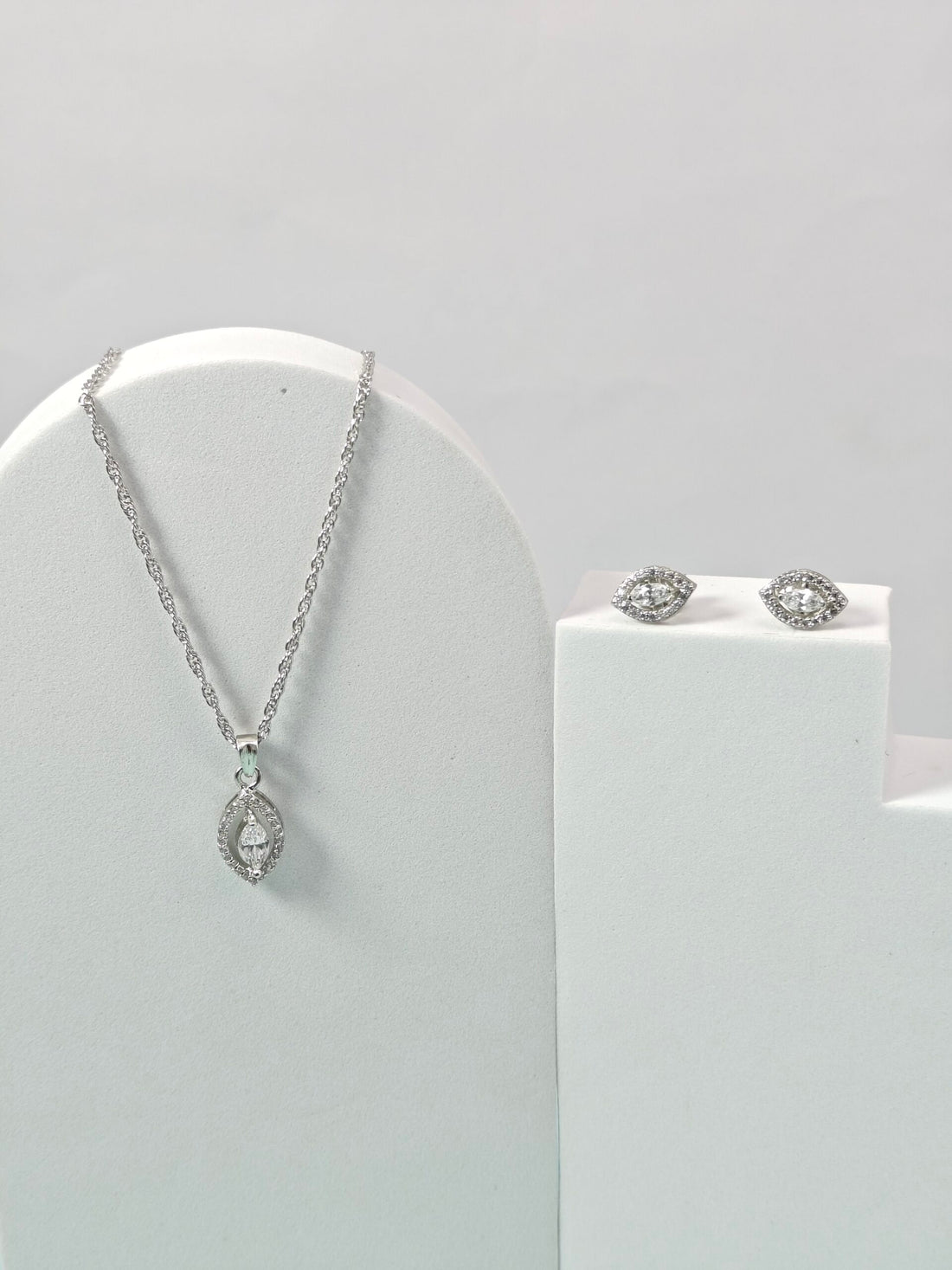 Silver necklace and earrings on a white stand against a light gray background
