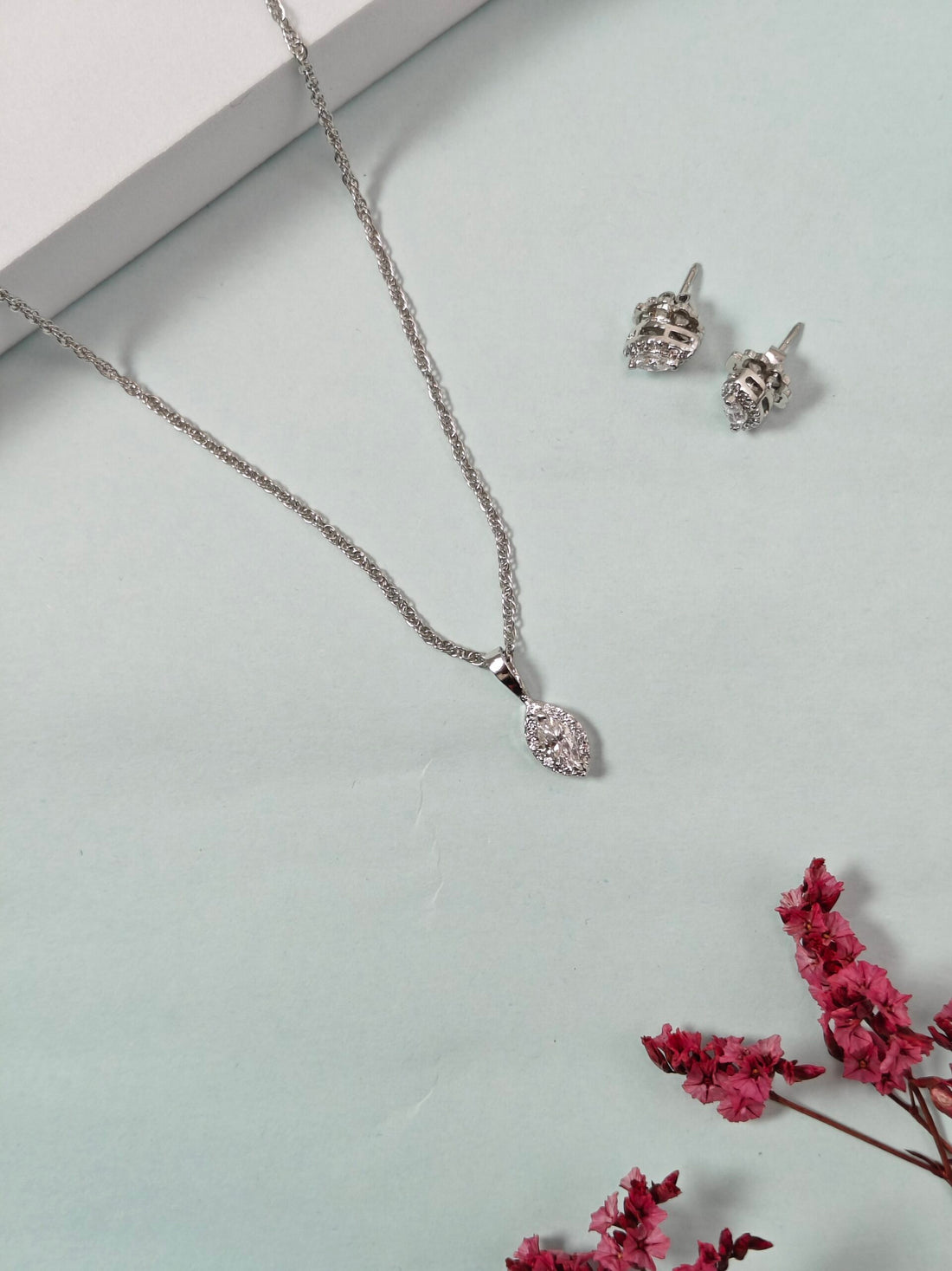 Silver necklace and earrings with pink flowers on a light gray background
