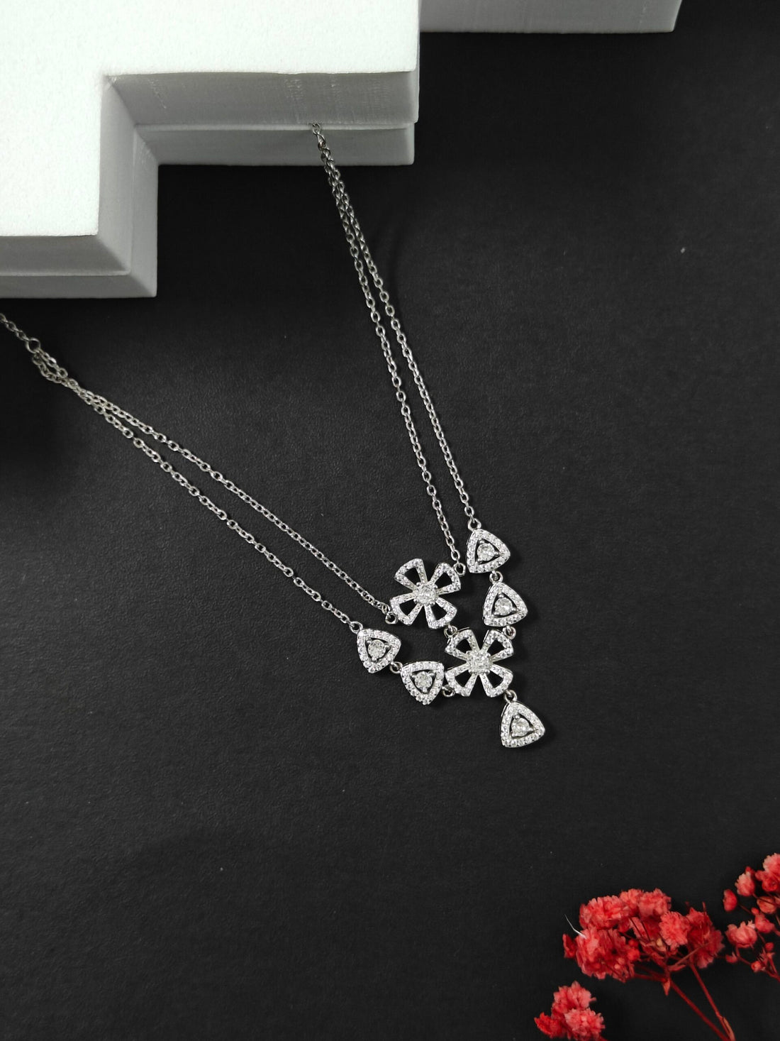 Silver necklace with floral pendant on a dark surface with red flowers